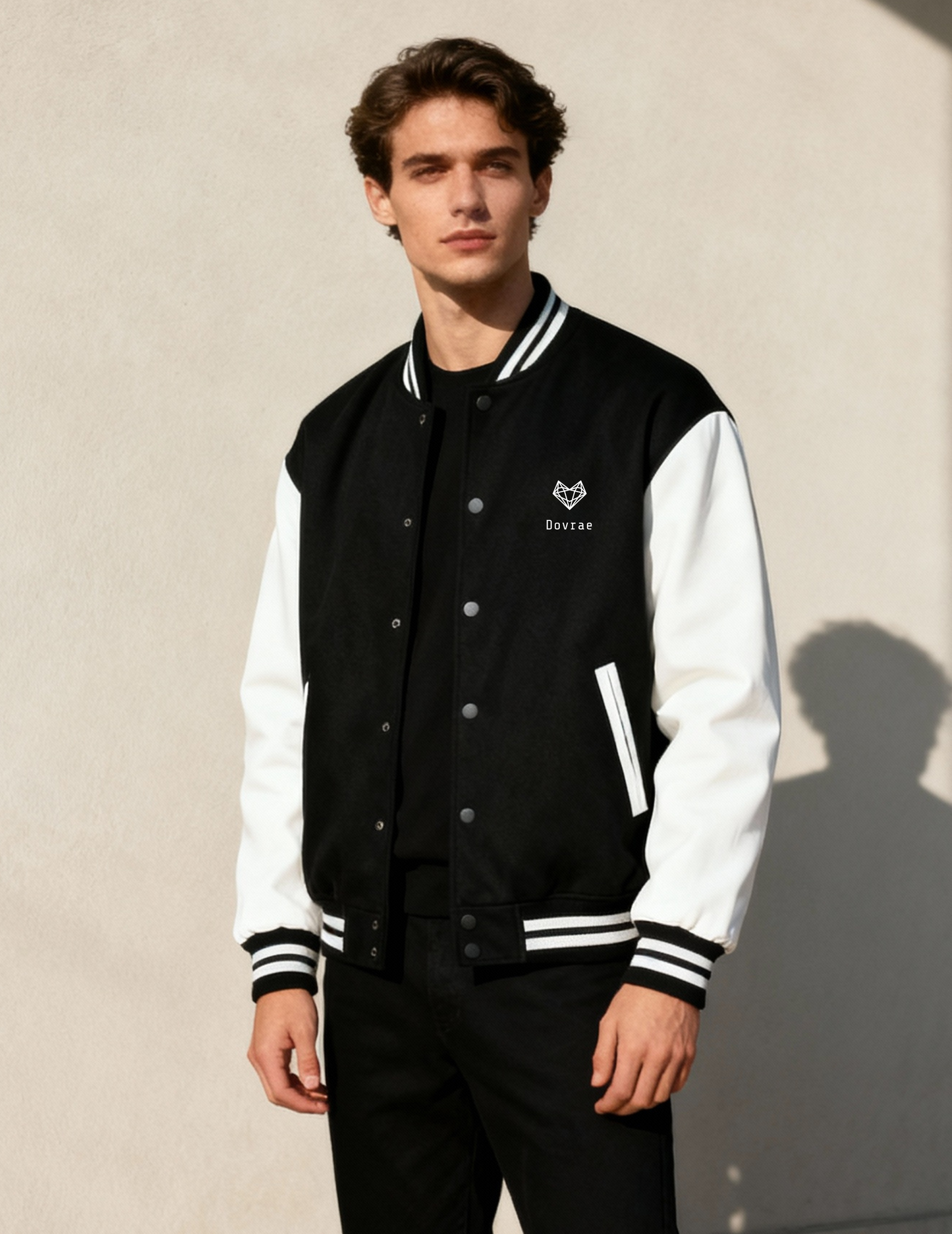 Man wearing a black and white varsity jacket with a logo on a beige background