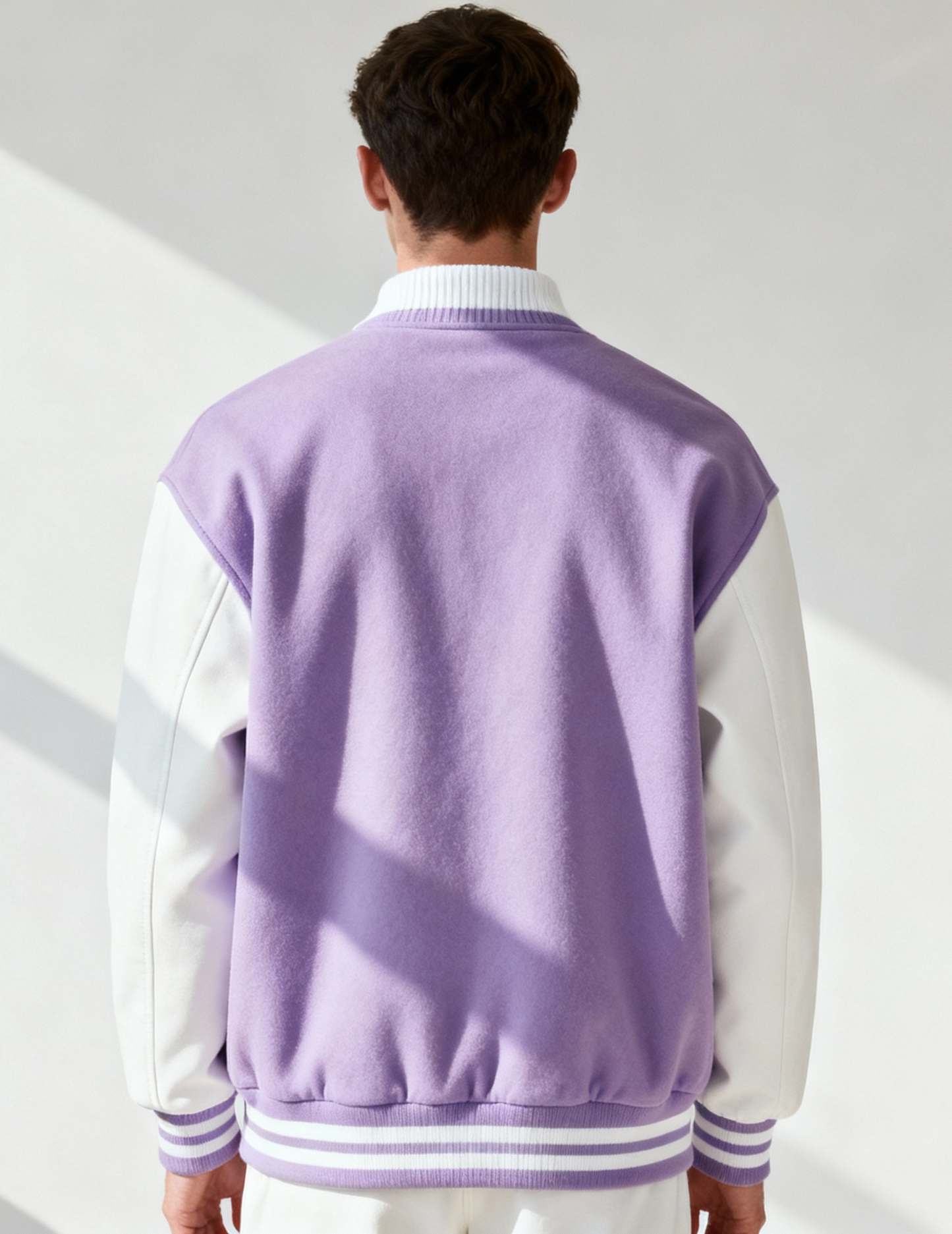 Person wearing a purple and white varsity jacket with a plain background