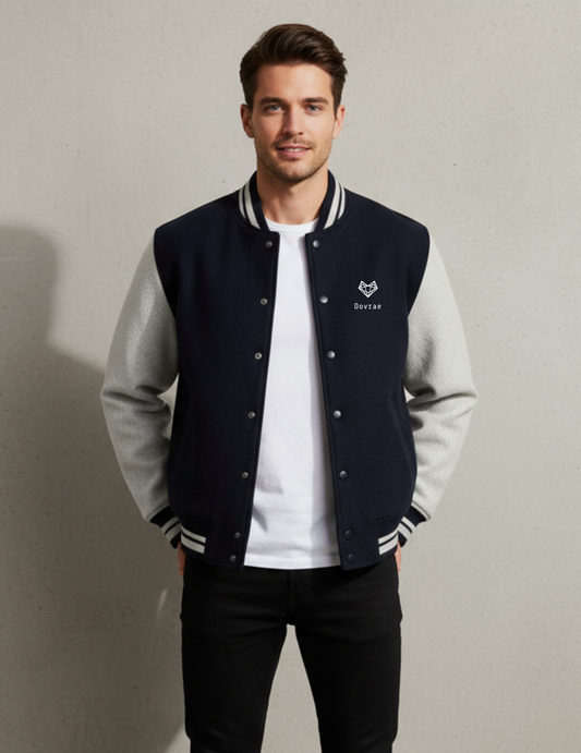 Man wearing a navy and gray varsity jacket with a white shirt underneath on a plain background